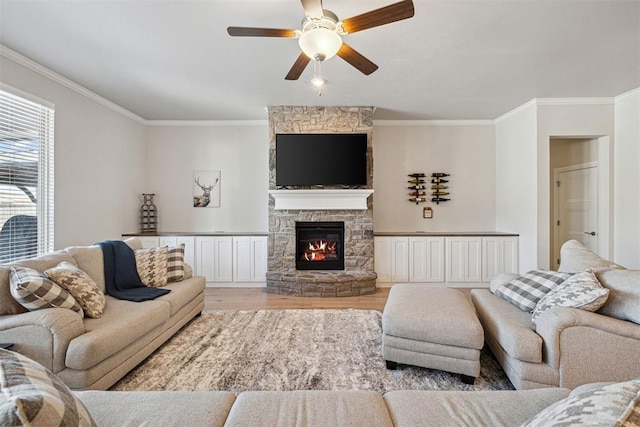 living area featuring a ceiling fan, a stone fireplace, crown molding, and light wood-style floors
