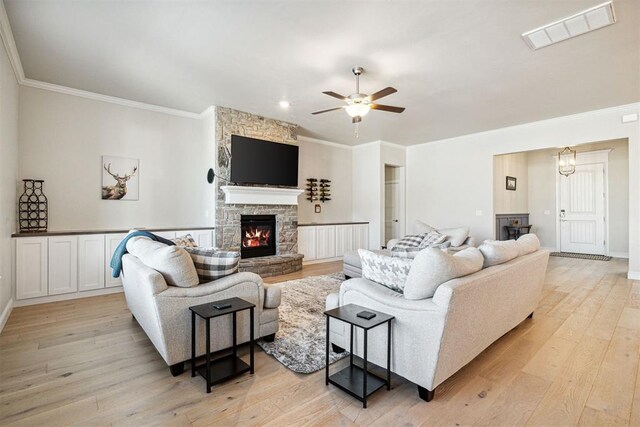living area featuring light wood-style flooring, visible vents, crown molding, a fireplace, and a ceiling fan