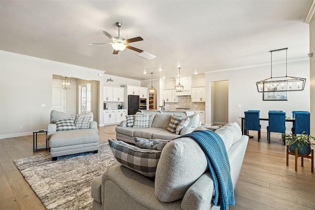 living room featuring baseboards, crown molding, light wood-type flooring, and ceiling fan with notable chandelier