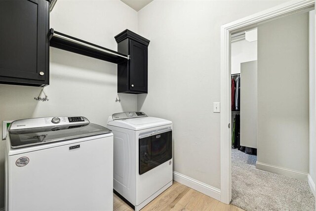 washroom featuring light wood-style flooring, baseboards, washing machine and clothes dryer, and cabinet space