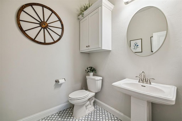 half bathroom featuring baseboards, toilet, and a sink