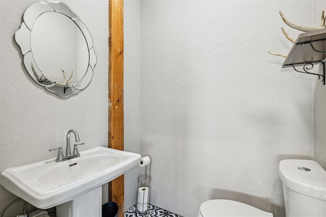 half bath featuring a textured wall, toilet, and a sink