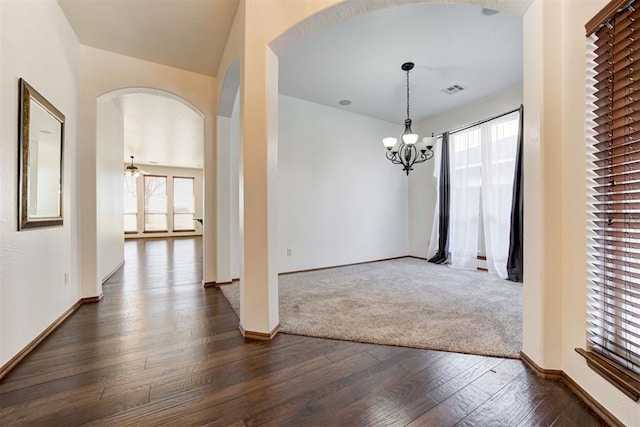 unfurnished dining area featuring visible vents, arched walkways, dark wood-type flooring, and a chandelier