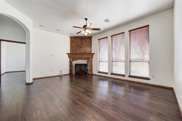 unfurnished living room featuring a ceiling fan, a large fireplace, visible vents, arched walkways, and dark wood-type flooring