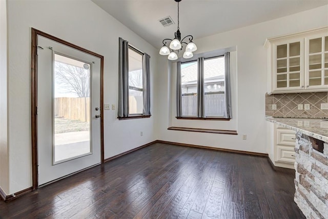 unfurnished dining area featuring dark wood-style floors, visible vents, baseboards, and an inviting chandelier