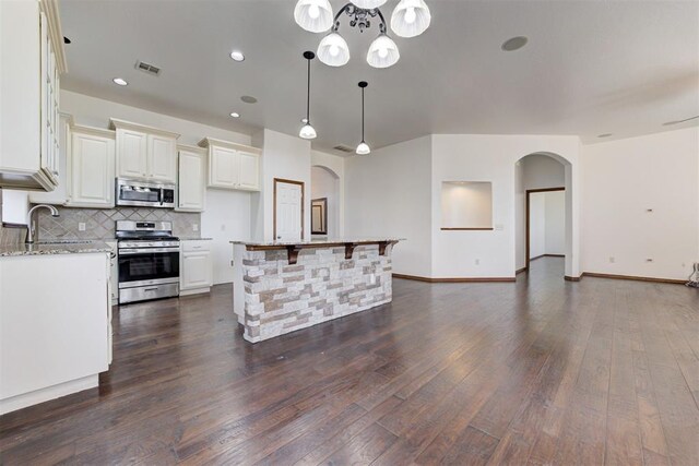 kitchen with dark wood-style flooring, stainless steel appliances, tasteful backsplash, arched walkways, and a sink
