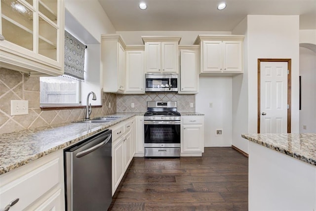 kitchen featuring a sink, dark wood-style floors, light stone countertops, appliances with stainless steel finishes, and glass insert cabinets