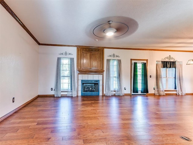 407 Heather Ln, Tuttle, OK 73089 - unfurnished living room featuring light wood-style flooring, crown molding, ceiling fan, baseboards, and a tiled fireplace