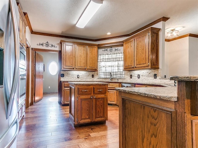 407 Heather Ln, Tuttle, OK 73089 - kitchen with crown molding, stainless steel appliances, brown cabinets, light wood-style floors, and a textured ceiling