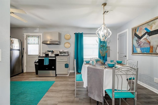 dining room with visible vents, baseboards, wood finished floors, and ceiling fan with notable chandelier