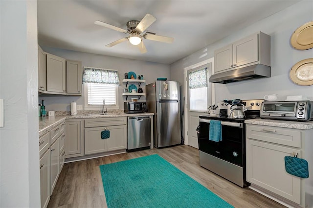 kitchen featuring a sink, light wood-type flooring, a ceiling fan, under cabinet range hood, and stainless steel appliances