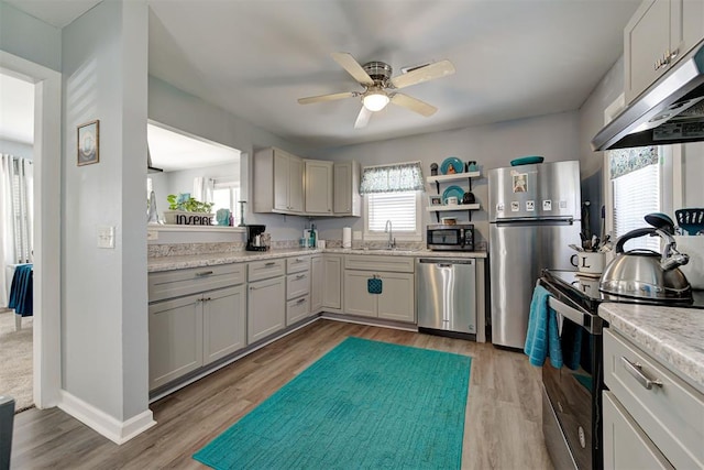 kitchen featuring a ceiling fan, under cabinet range hood, light wood-style floors, appliances with stainless steel finishes, and a sink
