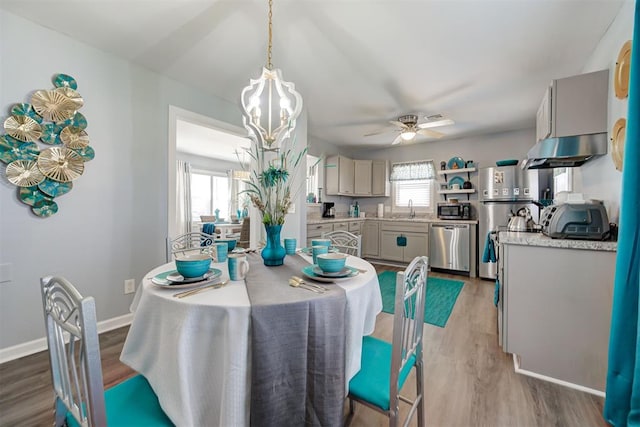 dining space featuring wood finished floors, ceiling fan with notable chandelier, and baseboards