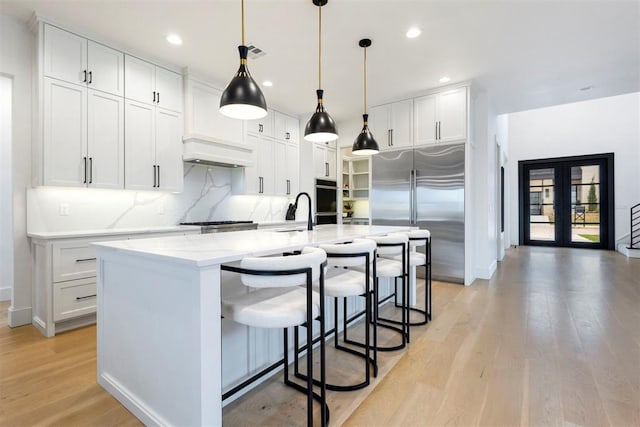 2109 Wiregrass Rd, Edmond, OK 73025 - kitchen with stainless steel built in refrigerator, decorative backsplash, white cabinetry, light wood-style flooring, and a kitchen breakfast bar