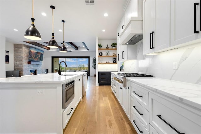 2109 Wiregrass Rd, Edmond, OK 73025 - kitchen with stainless steel appliances, light wood-style floors, open shelves, premium range hood, and white cabinetry