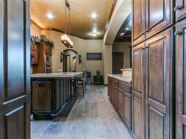 kitchen with arched walkways, ornamental molding, stainless steel appliances, wood-type flooring, and light countertops