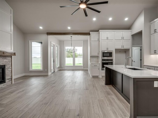 15216 Bedford Rd, Edmond, OK 73013 - kitchen with stainless steel oven, ceiling fan with notable chandelier, a sink, built in microwave, and light wood finished floors