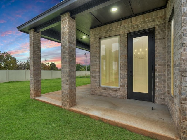 15216 Bedford Rd, Edmond, OK 73013 - view of exterior entry with a patio area, fence, brick siding, and a yard