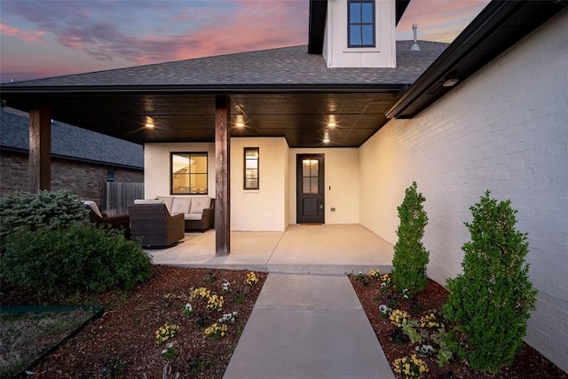 entrance to property with an outdoor living space, a shingled roof, and brick siding