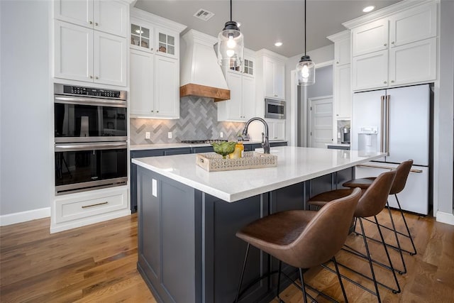 kitchen with stainless steel appliances, wood finished floors, baseboards, decorative backsplash, and custom range hood