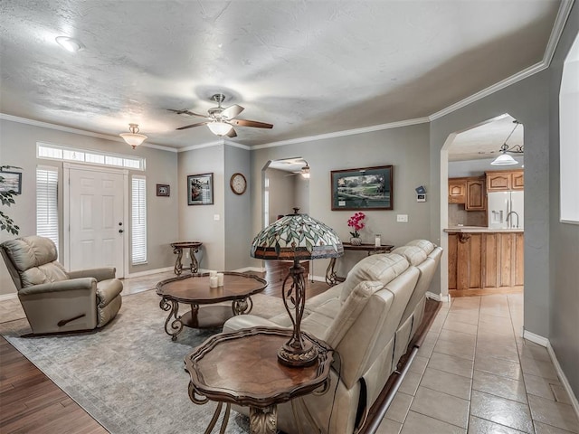 living area featuring ornamental molding, baseboards, arched walkways, and ceiling fan