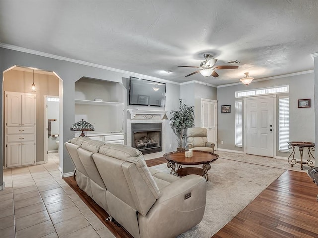 living room with a ceiling fan, baseboards, arched walkways, and crown molding