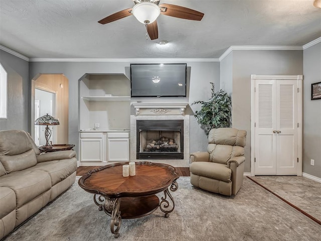 living area featuring ceiling fan, baseboards, ornamental molding, and a tiled fireplace