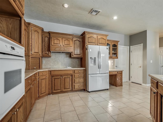 kitchen featuring brown cabinetry, visible vents, white appliances, and light countertops