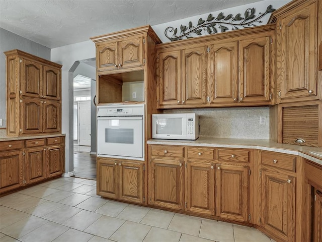 kitchen with arched walkways, light countertops, brown cabinetry, and white appliances