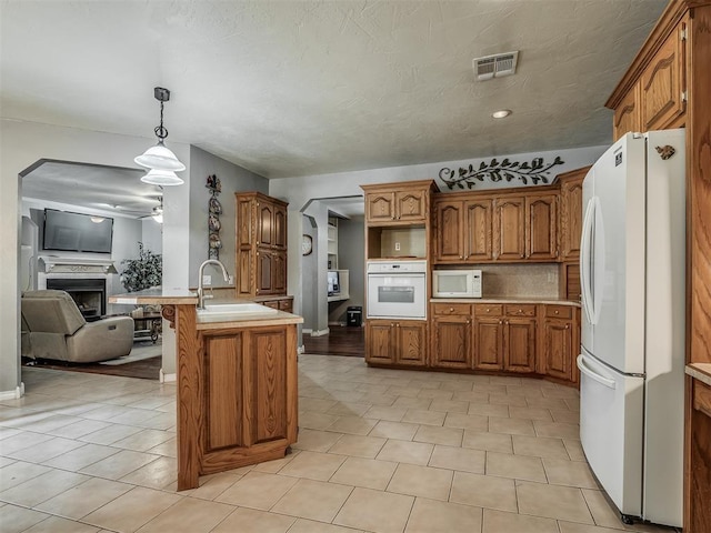 kitchen with a sink, visible vents, white appliances, brown cabinetry, and a fireplace
