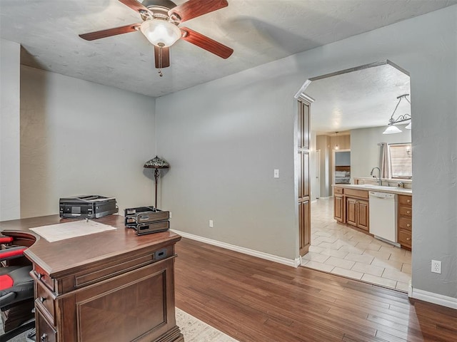 office space with a sink, light wood-type flooring, ceiling fan, arched walkways, and baseboards