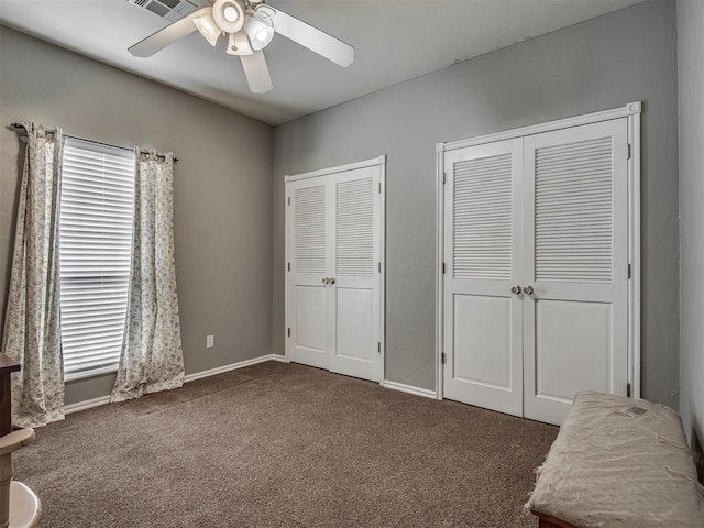 unfurnished bedroom featuring two closets, carpet floors, a ceiling fan, and baseboards