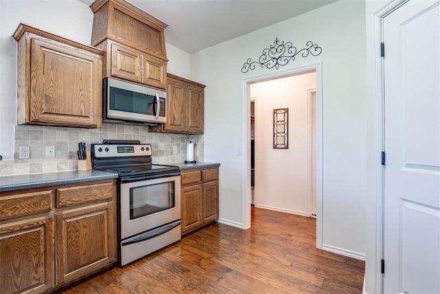 6574 Mint Julep Ln, Guthrie, OK 73044 - kitchen featuring appliances with stainless steel finishes, backsplash, dark wood-style flooring, dark countertops, and brown cabinets
