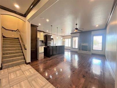 708 Kearny Ln, Yukon, OK 73099 - unfurnished living room with ceiling fan, dark wood-style flooring, a fireplace, stairs, and ornamental molding