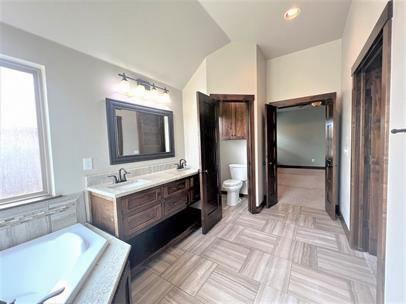 708 Kearny Ln, Yukon, OK 73099 - bathroom featuring double vanity, a bath, and vaulted ceiling