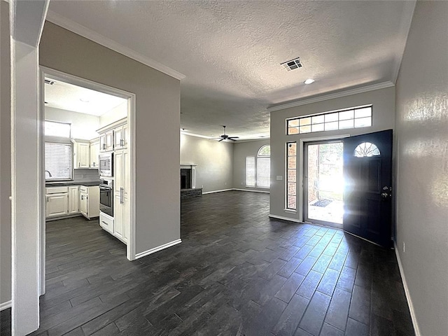 713 NW 143rd St, Edmond, OK 73013 - foyer featuring ceiling fan, crown molding, dark wood finished floors, a textured ceiling, and a fireplace with raised hearth