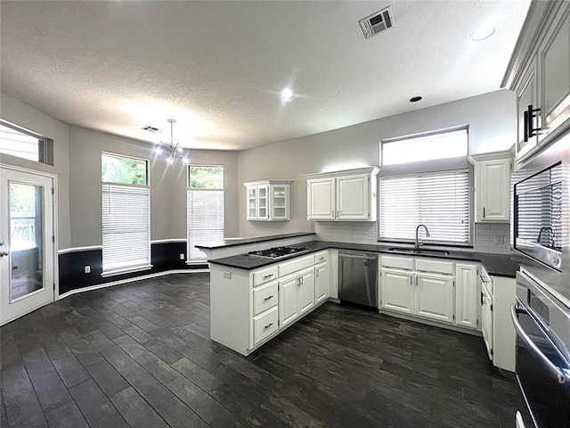 713 NW 143rd St, Edmond, OK 73013 - kitchen with appliances with stainless steel finishes, a peninsula, dark countertops, dark wood-type flooring, and a textured ceiling