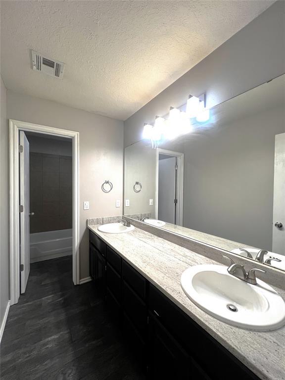 713 NW 143rd St, Edmond, OK 73013 - full bathroom featuring double vanity, wood finished floors, and a textured ceiling