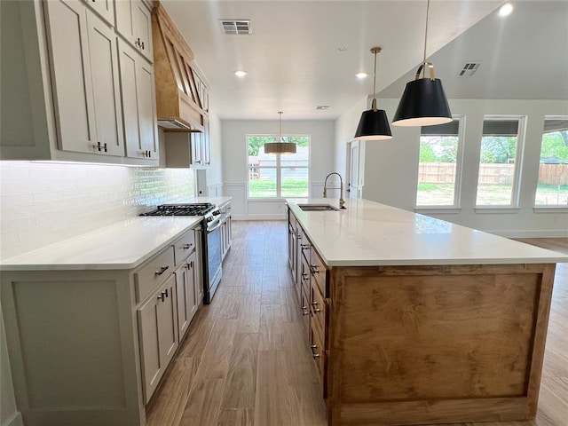 kitchen with gas stove, a sink, light wood finished floors, a spacious island, and backsplash