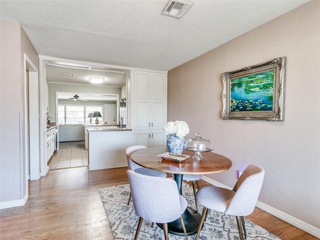 dining room with light wood-style floors, baseboards, a ceiling fan, and visible vents
