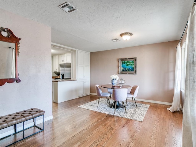 dining space featuring visible vents, baseboards, light wood finished floors, and a textured ceiling