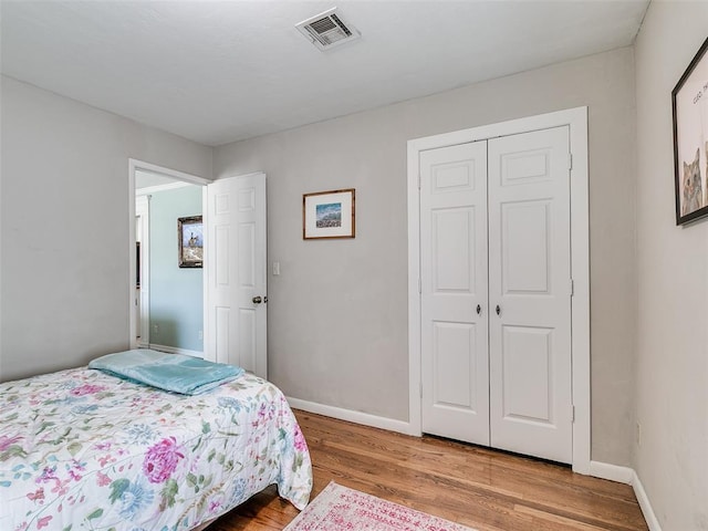 bedroom featuring visible vents, baseboards, a closet, and wood finished floors
