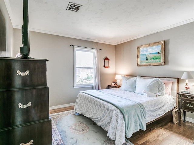 bedroom featuring visible vents, baseboards, crown molding, and wood finished floors