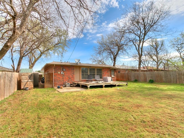 back of property featuring a lawn, a fenced backyard, a deck, and brick siding