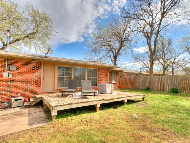 rear view of property featuring brick siding, a deck, fence, and a lawn