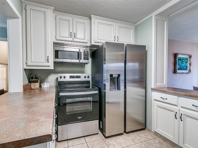 kitchen with stainless steel appliances, light tile patterned floors, white cabinetry, and a textured ceiling
