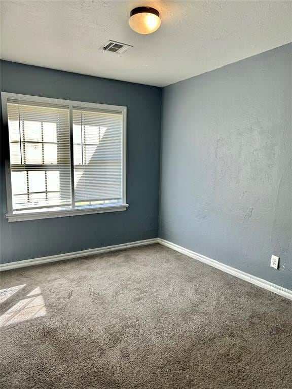 carpeted spare room featuring a textured ceiling, baseboards, and visible vents