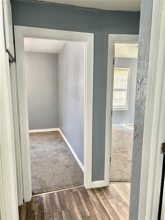 hallway featuring baseboards, wood finished floors, and carpet