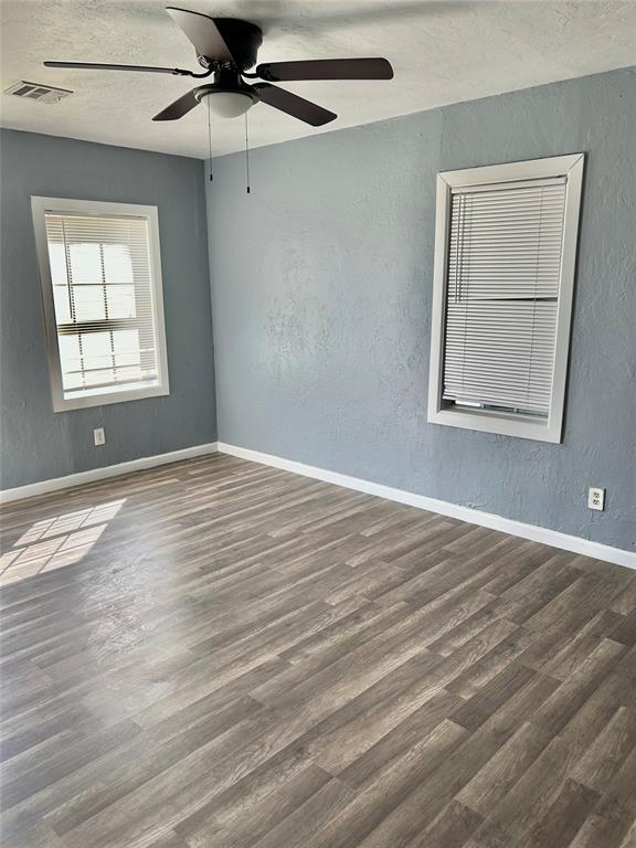 spare room with visible vents, wood finished floors, ceiling fan, and a textured wall