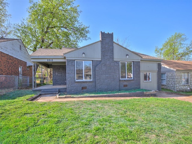 back of house with stone siding, a yard, a shingled roof, and fence